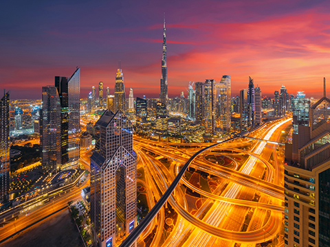 The Dubai skyline at dusk, the Burj Khalifa above a lit motorway interchange